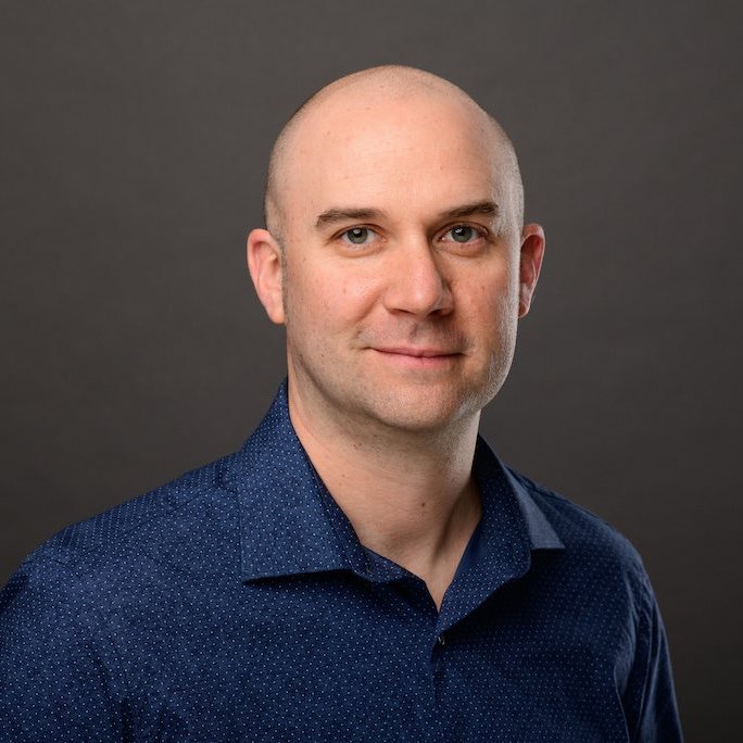 Headshot of Brian Cole wearing a navy blue dress shirt with small white polkadot detail.