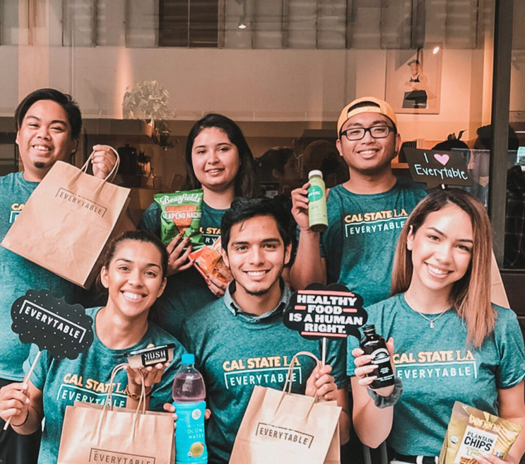 Group of smiling student volunteers holding Everytable meals, snacks, and drinks.